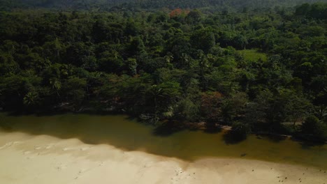 Epic-aerial-of-a-river-flowing-along-the-coastline-with-mountains-and-forest-in-the-background