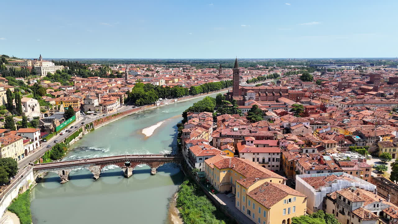 Aerial drone view of Verona's historic center with the Adige River winding through the city. A stone bridge crosses the river near terracotta rooftops and medieval towers
