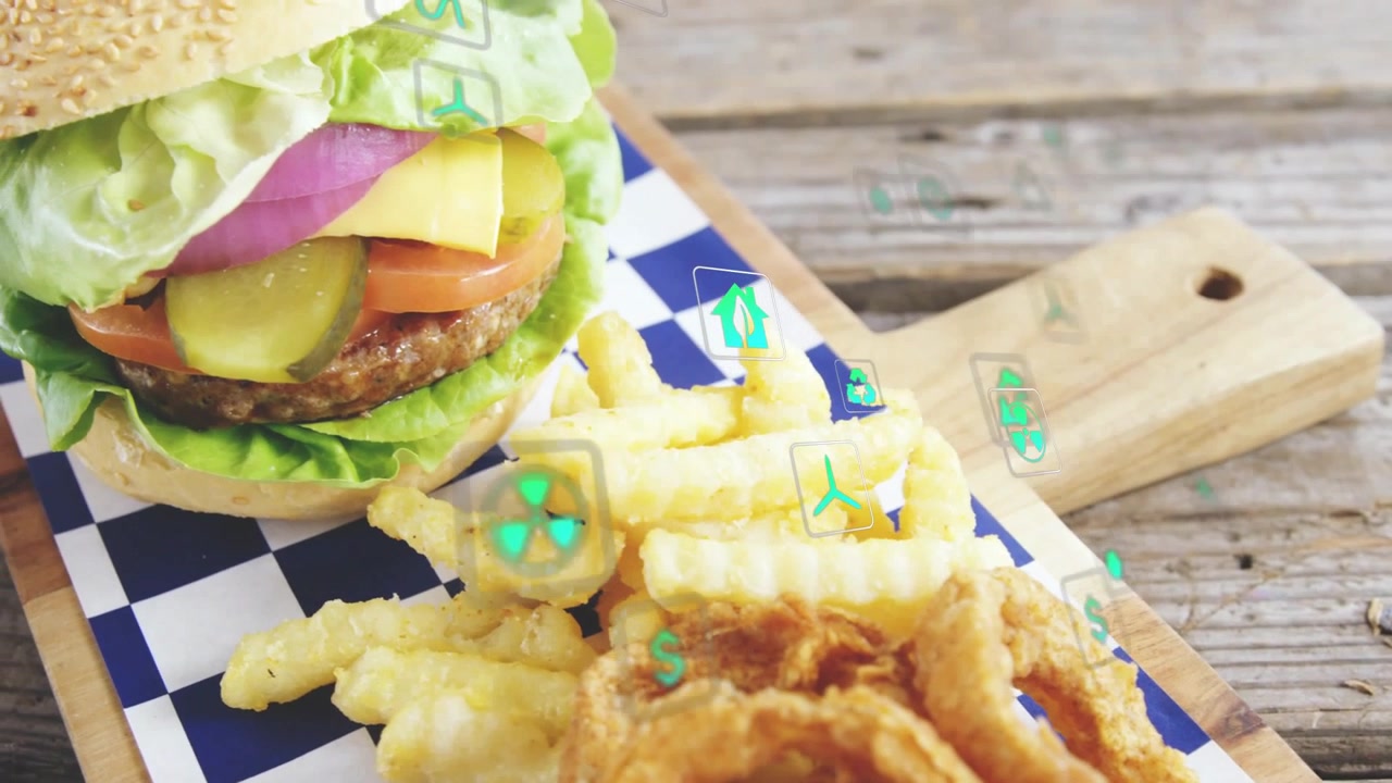 La telecamera si avvicina rivelando un hamburger su un tagliere, patatine fritte, anelli di cipolla, icone verdi che fluttuano, promuovendo il menu.