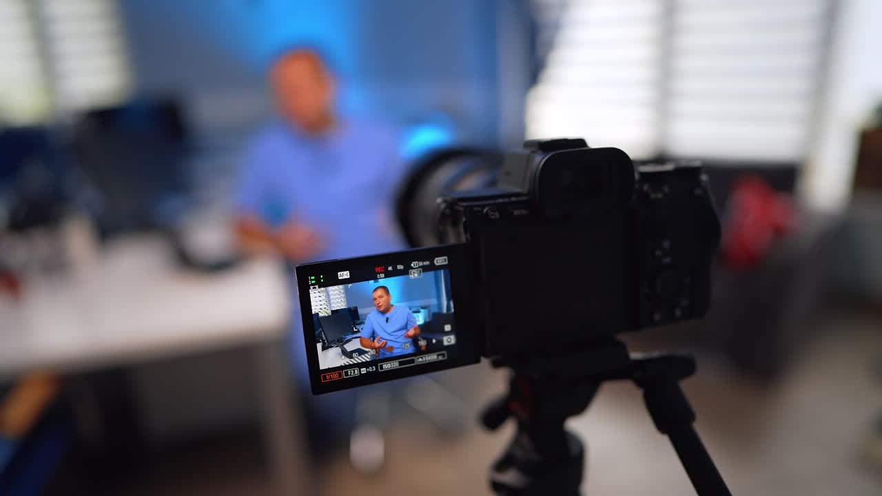 Caucasian doctor in blue uniform sits at desk talking. Medic creates a video vlog in his office. Selective focus