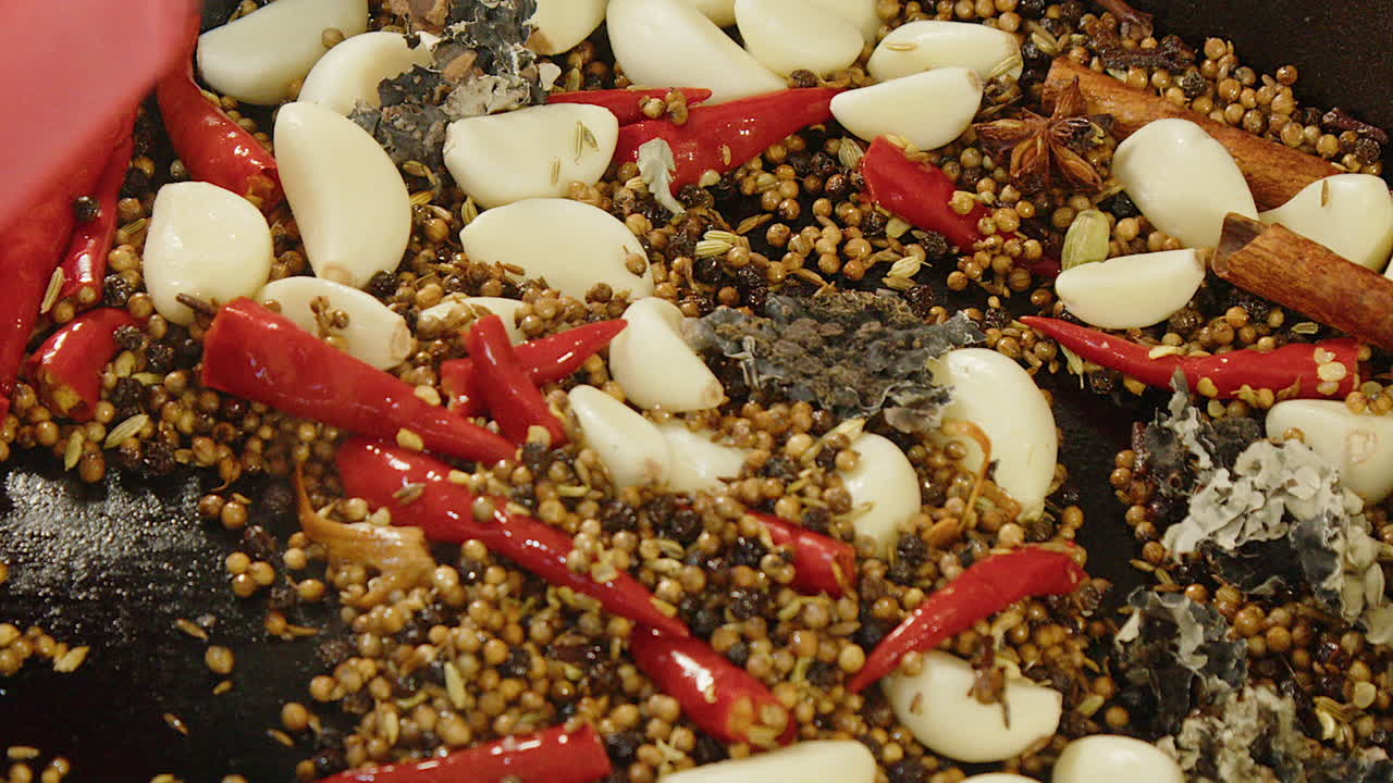 Primo piano: aglio e peperoncino piccante mescolati a spezie intere nella padella per masala