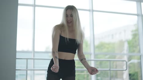 fit girl in black clothes performing contemporary. female dancer shows flowing motions, body and hands waves at white room. modern ballet dance choreography. young woman is moving smoothly