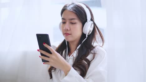 매력적인 캐주얼 아시아 여성 성인 여성 음악 듣기 헤드폰 긍정적 인 감정 창 에 바닥에 앉아 즐거움과 평화로운 웃음 편안,아시아 여성은 집에서 스마트폰을 사용 낮에 캐주얼