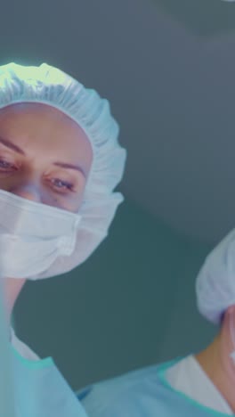 female surgeon in surgical mask and cap focused on patient during operation in sterile environment