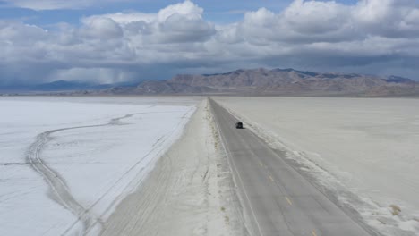 car traveling on long straight and narrow road in desert, aerial follow