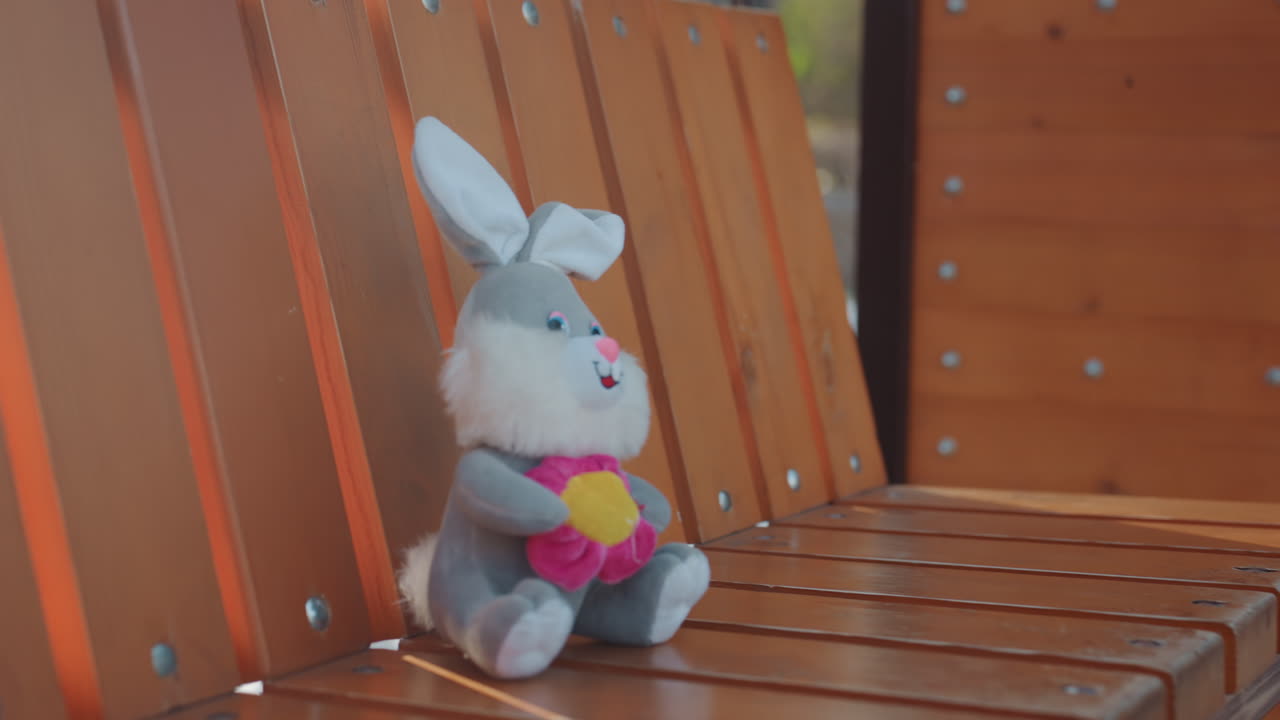 Blid legetøjsscene. Fredelig eftermiddag med legetøjsarrangement. Stille parkscene med plysbunny og nedgående sol. Rolig udendørsscene med blød plyskanin, der soler sig i det falmende aftenlys