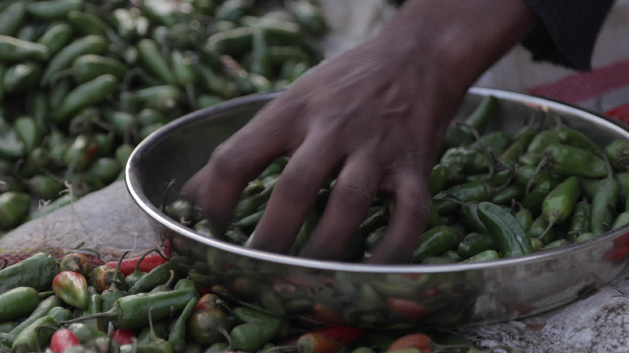 mercado africano, mujer agarra chiles jalapeños shishito del tazón, cierra la mano