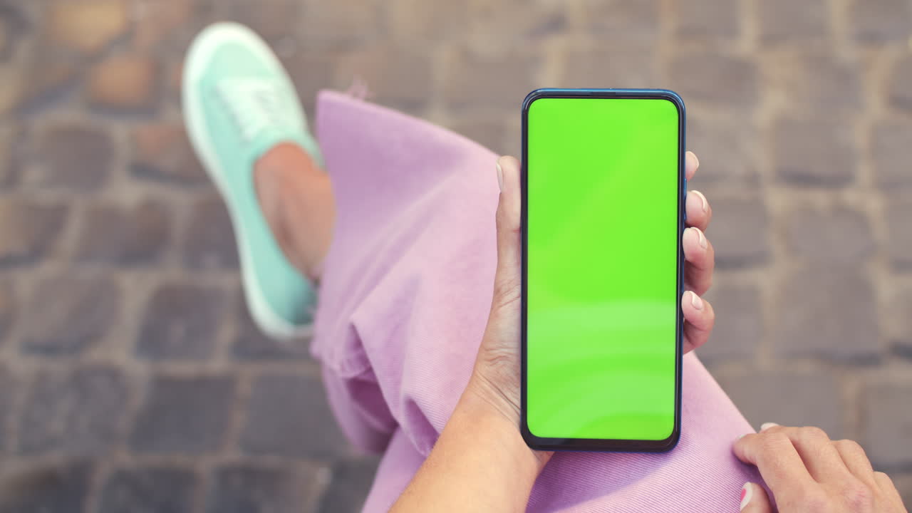 Person holding a smartphone with a green screen display outdoors