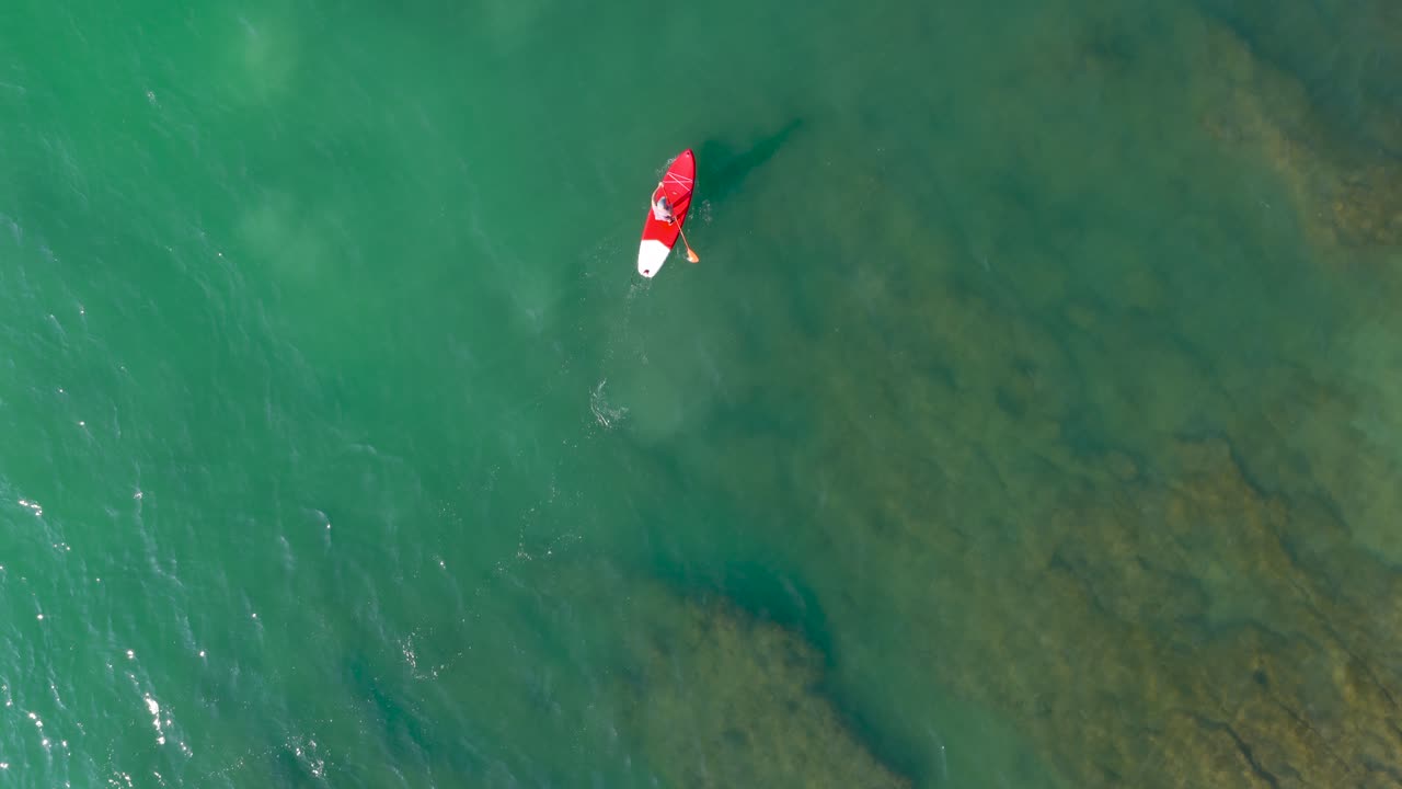 Lifeguard paddling on red paddleboard in clear water