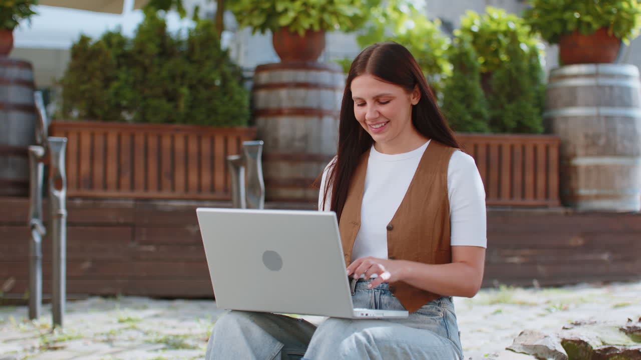 joven caucásica freelance trabajando en línea trabajo remoto con computadora portátil sentado en la calle de la ciudad