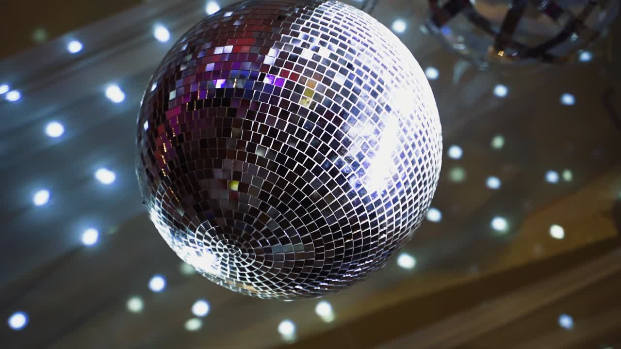 Round mirror ball shimmering. Shining disco ball hanging on the ceiling and rotating at nightclub. Close-up.