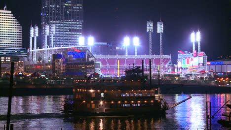 La-Luz-Se-Refleja-En-El-Río-Ohio-Con-La-Ciudad-De-Cincinnati,-Ohio,-El-Fondo-Como-Un-Barco-Fluvial-Pasa-Por-Debajo-1