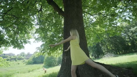 woman in yellow dress dancing by tree in summer park