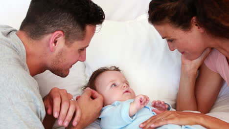 Baby-boy-in-blue-babygro-being-tickled-by-parents-on-bed