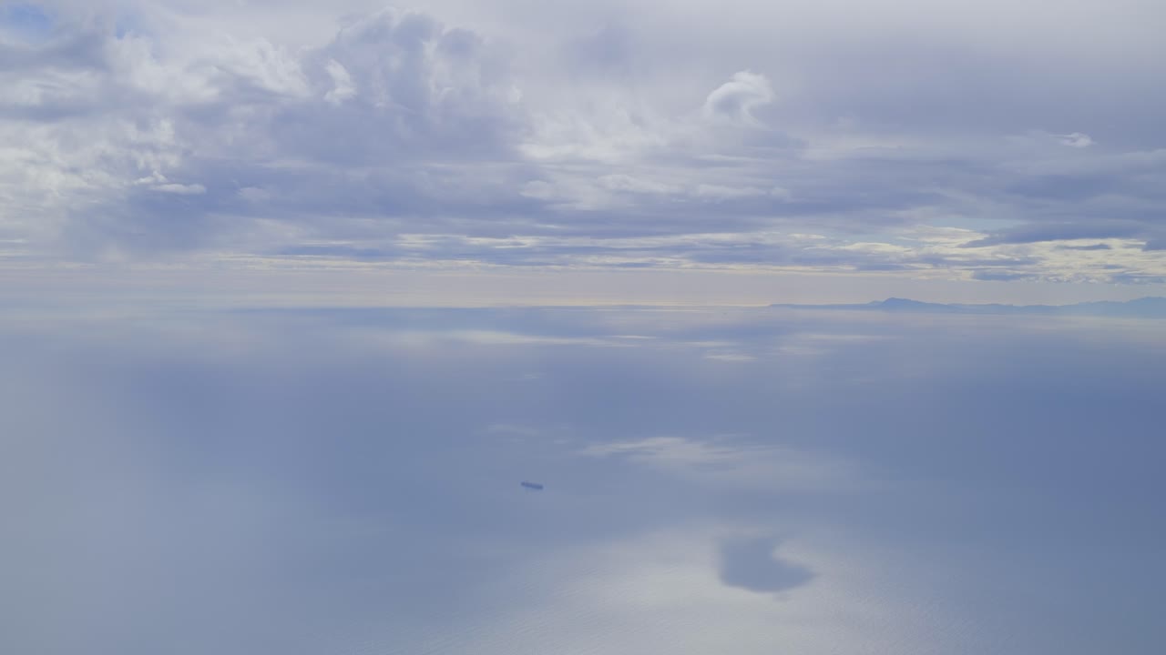 Calm sea view with a cargo ship under a cloudy sky, distant land on the horizon