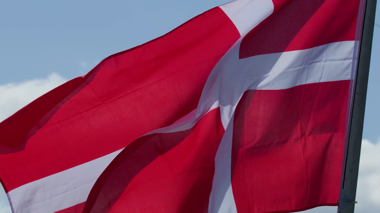 Et levende rødt og hvidt dansk flag blafrer dynamisk i et nærbillede udendørs.