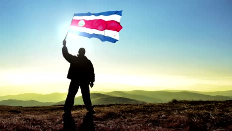 successful silhouette man winner waving costa rica flag on top of the mountain peak. cinemagraph loop background