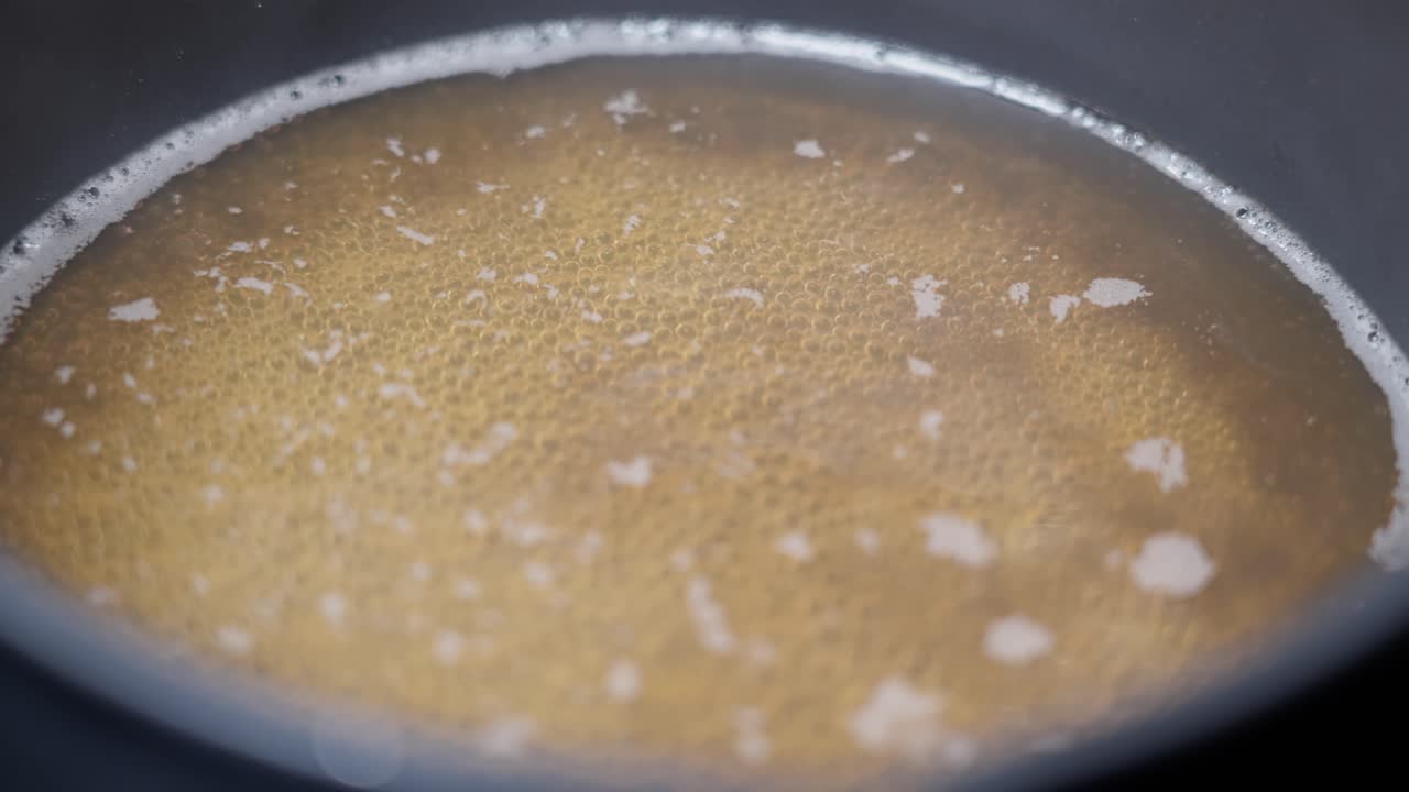 Fresh golden bone broth simmering in pan, close up