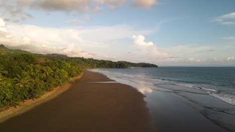 drone, wide shot, moving round, across sandy beach with tranquil waves trees