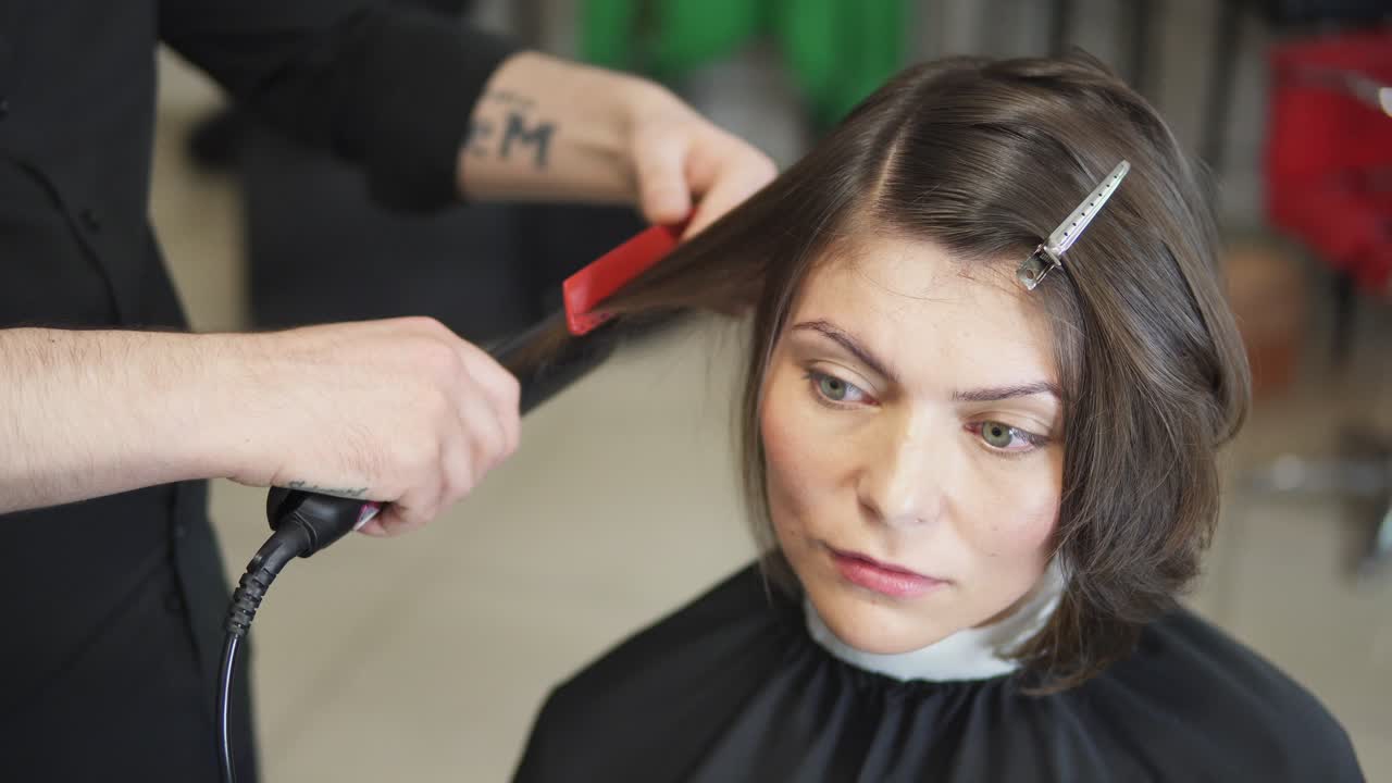 Professional hairdresser, stylist makes professional hairstyle of young woman in beauty studio, using barrette for fixing hairdo. Hair straightening Beauty and haircare concept