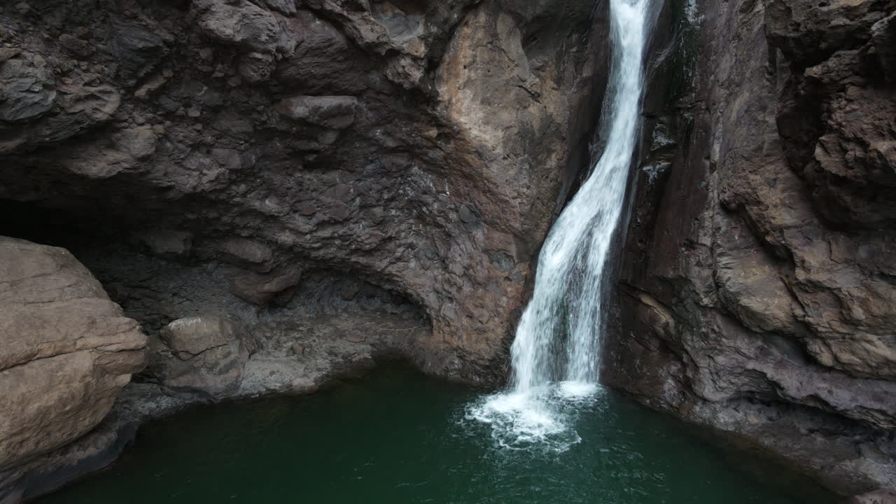 Water falling down a rocky ravine into a secluded green pool at Charco ...