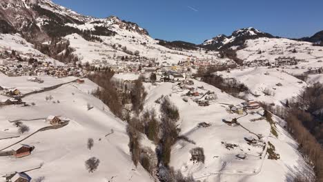 stunning drone push in to amden, swiss alps in winter, snowy peaks, alpine village rooftops and serene mountain landscape near walensee and glarus.