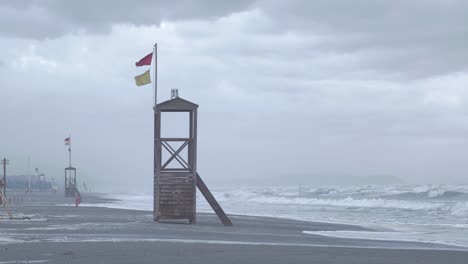 una torre de salvavidas vacía en un triste día gris en la playa mientras el viento sopla las banderas rojas y amarillas