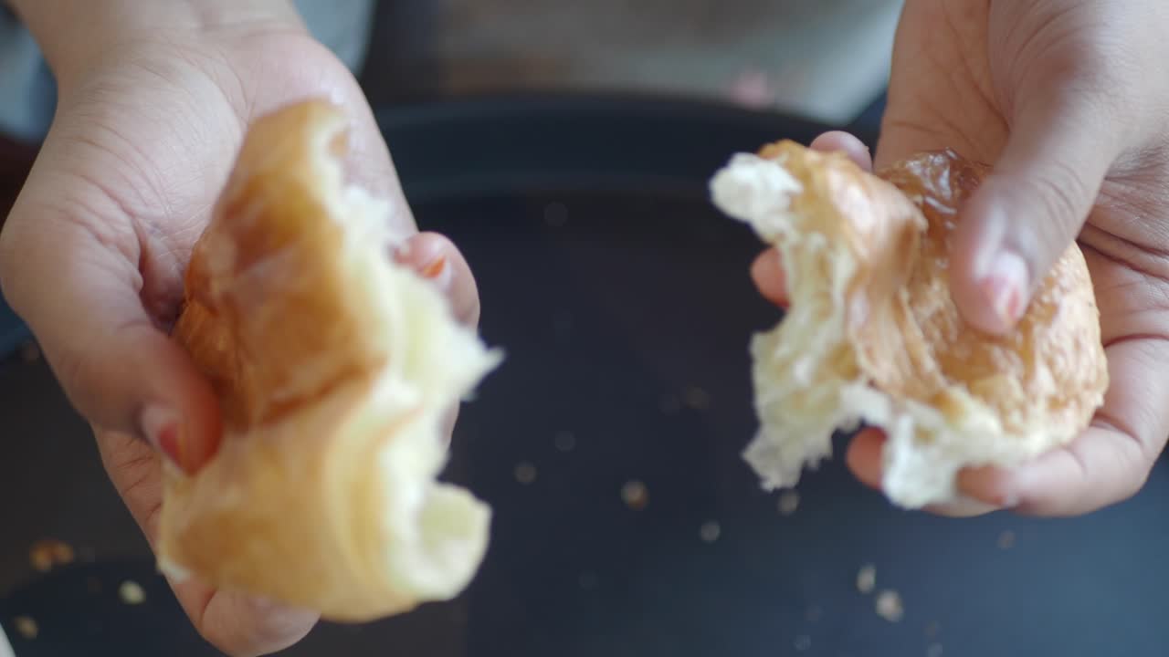 Woman tearing a croissant in half