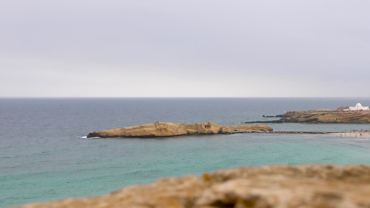 Rocky island in blue sea and horizon in cloudy sky on background. DOF effect