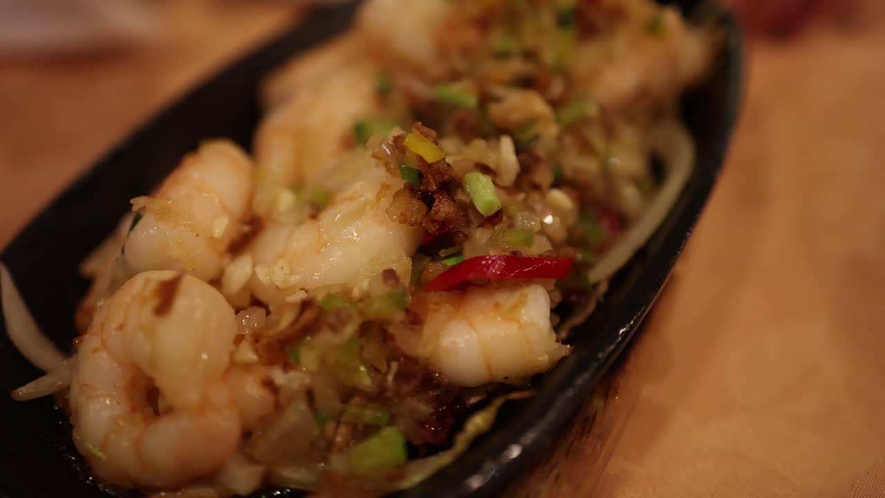 Close-up of steaming prawn and vegetable rice dish on black plate, warm indoor lighting