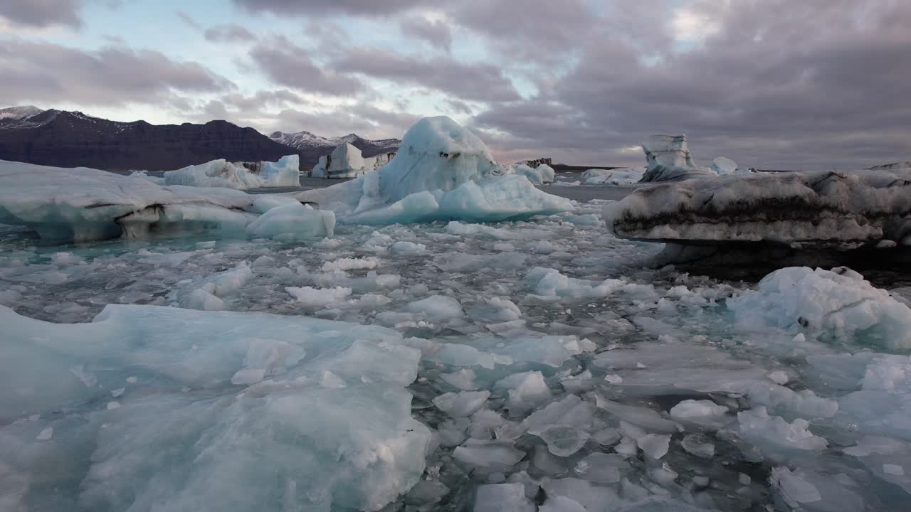 Cinematic low aerial backwards away from iceberg over ice floes in the arctic