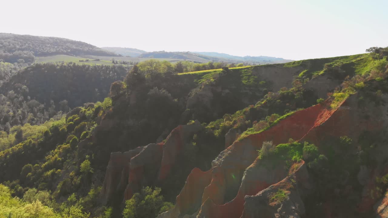 Vista aerea di un canyon di roccia rossastra spettacolare con vegetazione verdeggiante tra le dolci colline toscane