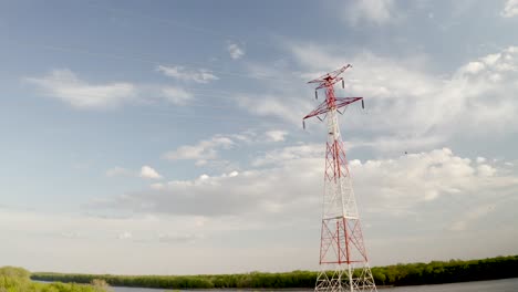 Drone-arial-of-transmission-tower-electrical-grid-power-lines-over-river-pretty-blue-sky-sunset