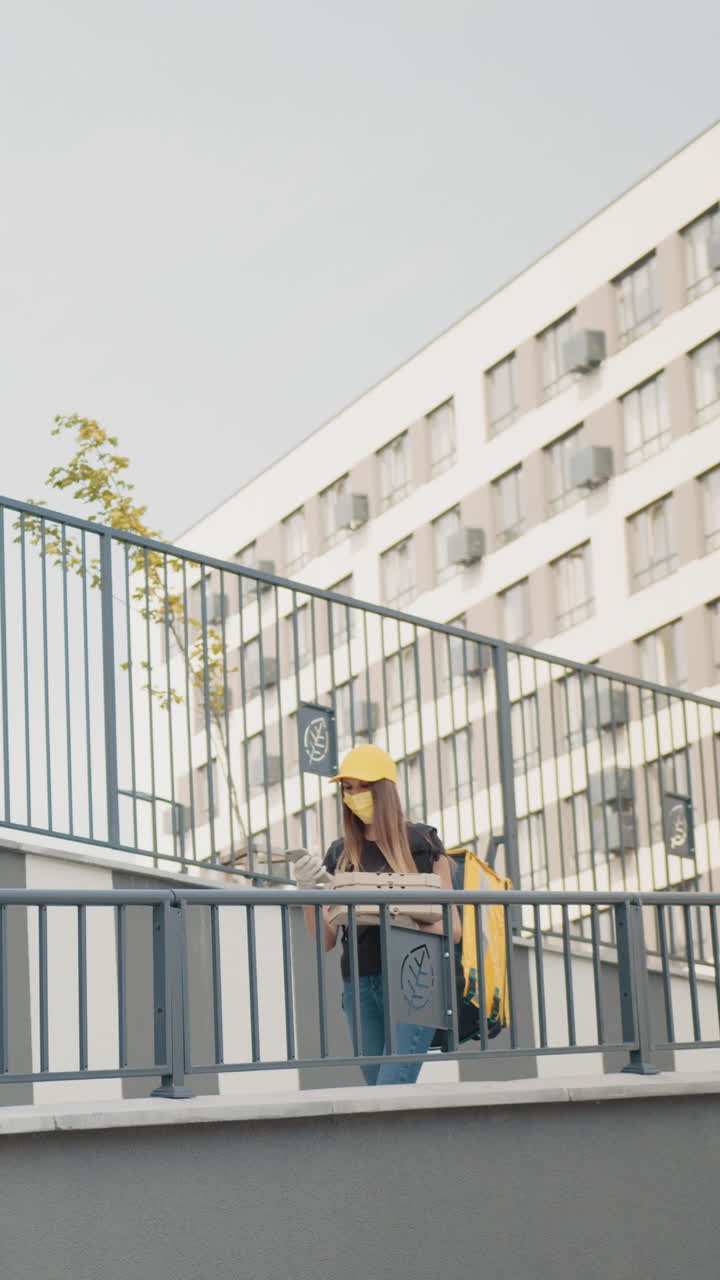 Delivery person wearing a mask and cap stands in front of a building