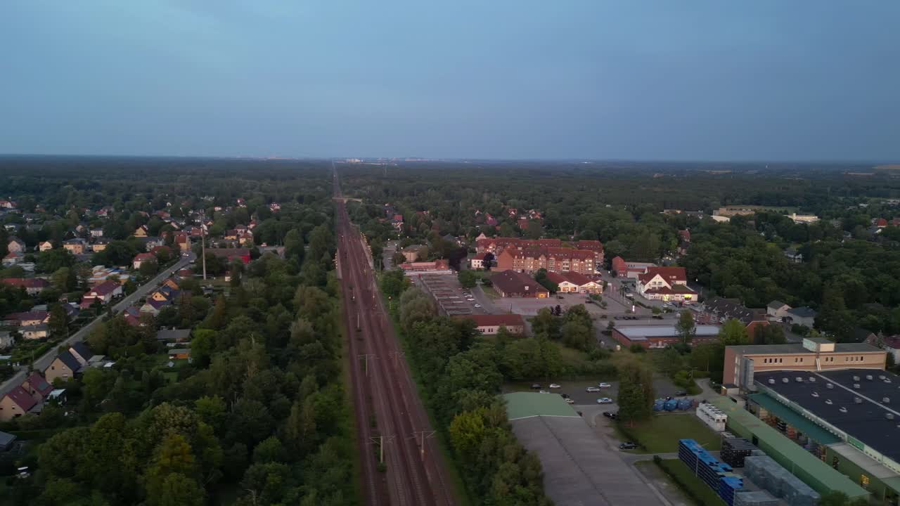 저녁에 작은 마을과 숲을 가로질러 철도에서 여행하는 여객 열차. 웅장한 공중 전망 비행 도리 왼쪽 드론