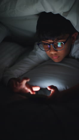 Vertical-Video-Close-Up-Of-Young-Boy-In-Bedroom-At-Home-Using-Mobile-Phone-To-Text-Message-Under-Covers-Or-Duvet-At-Night-6