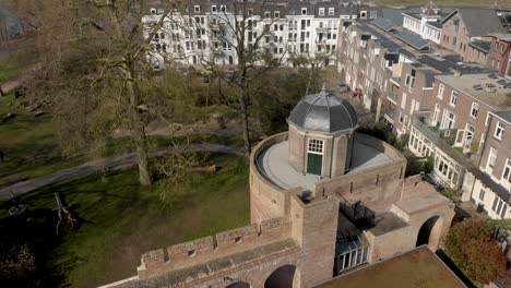 slow backwards aerial revealing top of historic ruins of bourgonje stronghold tower and city wall with remaining cants and arches before a park landscape in zutphen, the netherlands