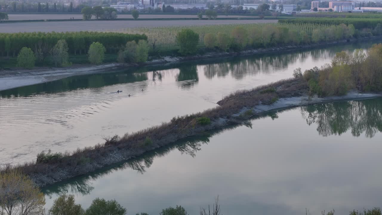 Drone view captureing Maginot bodri—a vegetated strip dividing twin Po River channels—near Cremona, with calm water, riparian trees, and distant fields under soft sunrise light