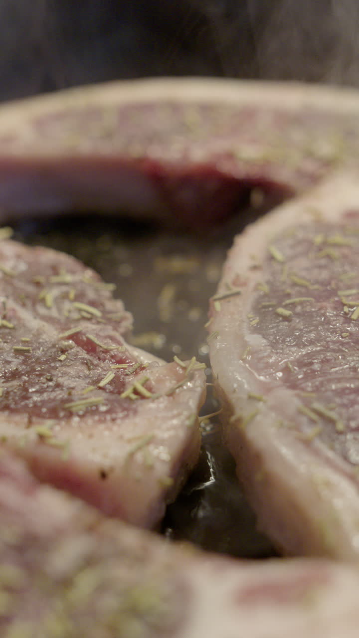 Juicy seasoned lamb chops sizzling in frying pan, close-up slider shot. Vertical