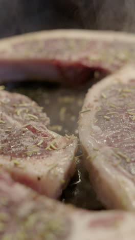 juicy seasoned lamb chops sizzling in frying pan, close-up slider shot. vertical