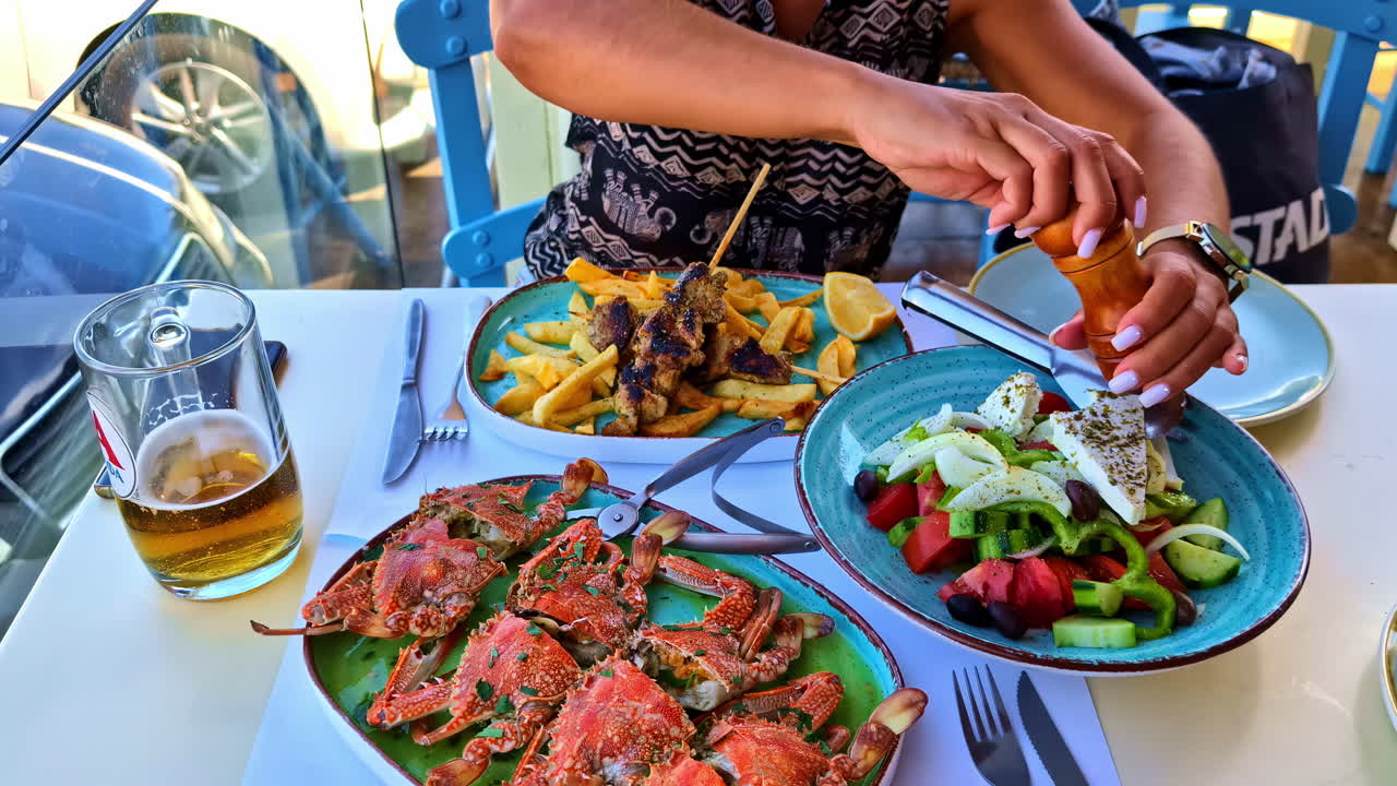 Woman adding salt and pepper to a delicious crab dish with vegetables and beer at a coastal restaurant