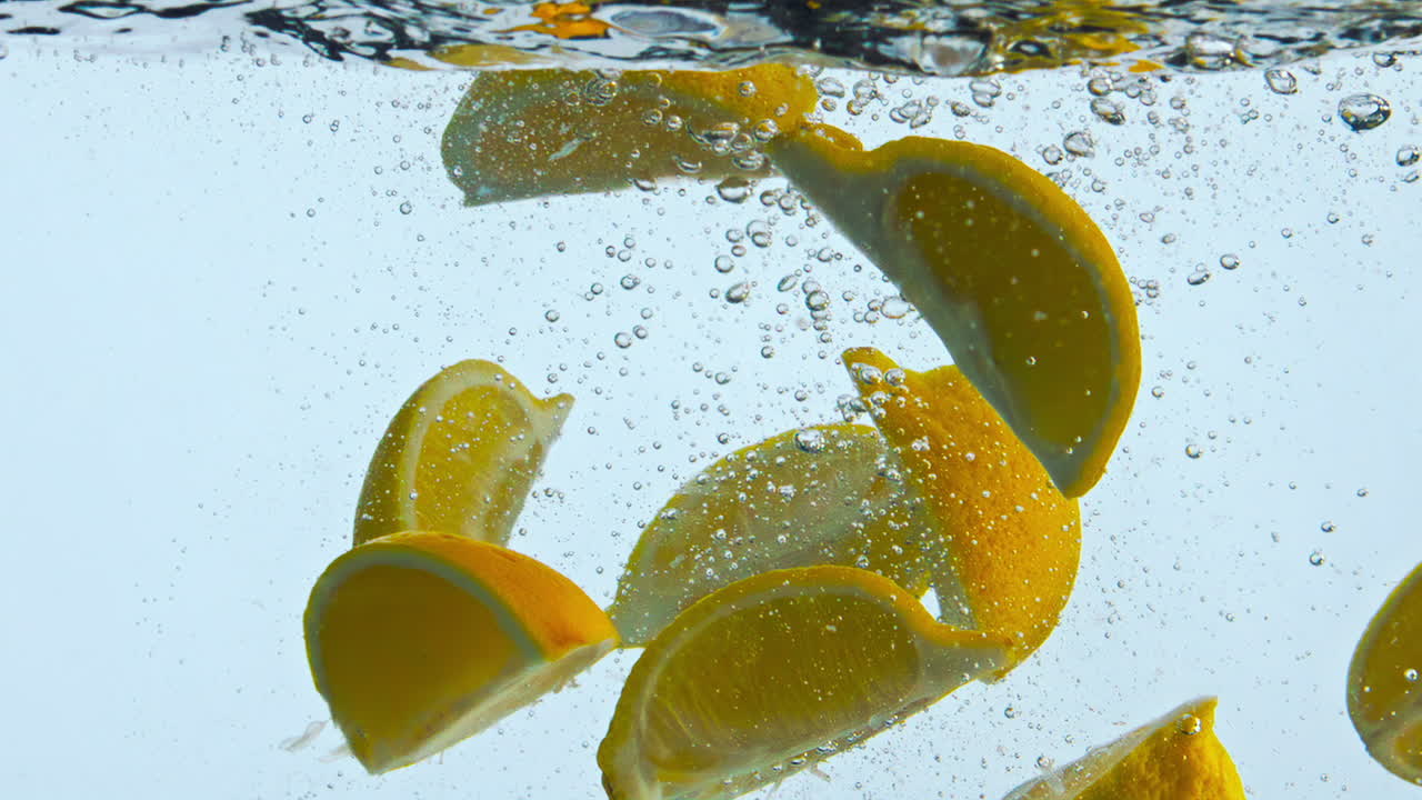 Dropping orange slices liquid close up. Citrus wedges raising to water surface