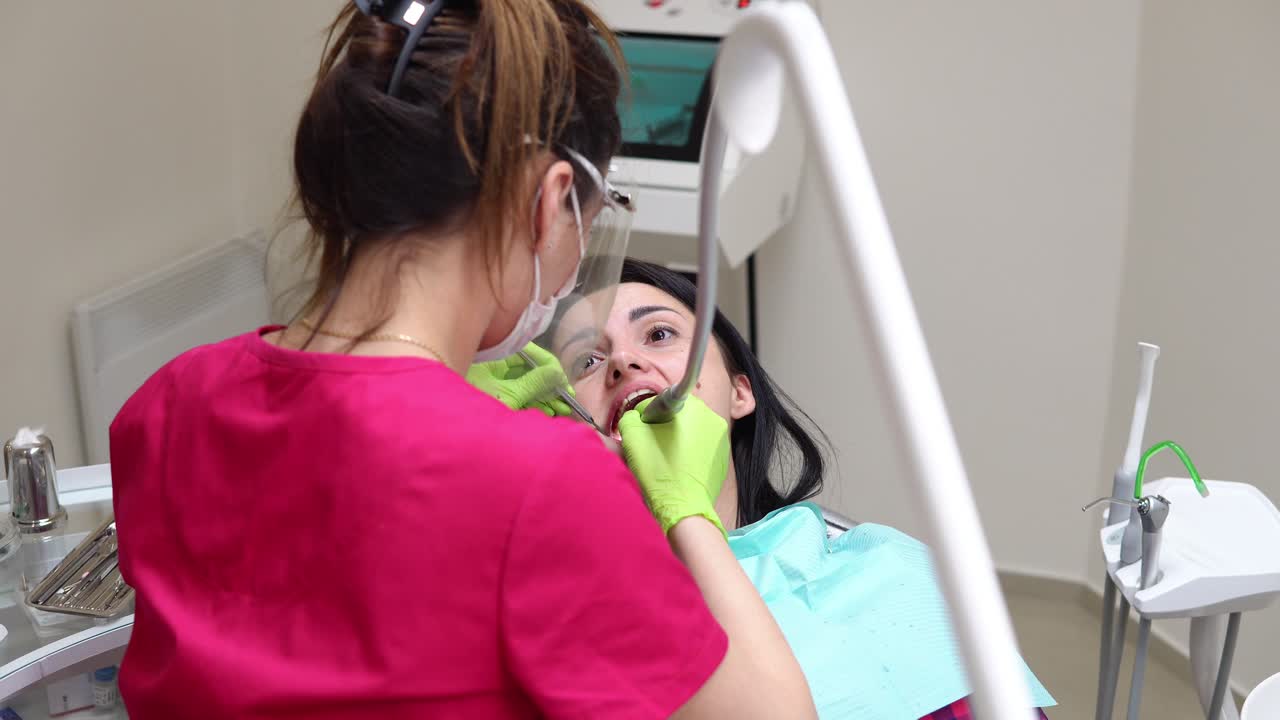 Dentist cleans woman's teeth with professional toothpaste and automatic brush. Dentist using saliva ejector or dental pump to evacuate saliva.