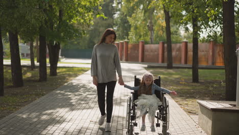 mother and little daughter in wheelchair enjoy walk in park