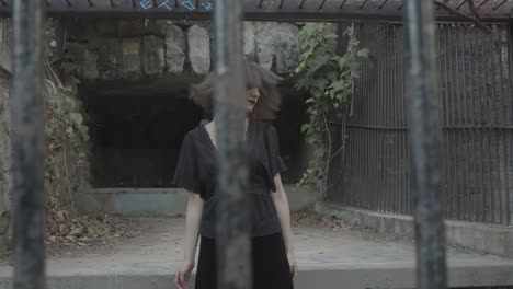 슬로우 모션 젊은 여성이 버려진 동물원 케이지의 금속 케이지 안에서 머리를 좌우로 흔들고 있습니다.