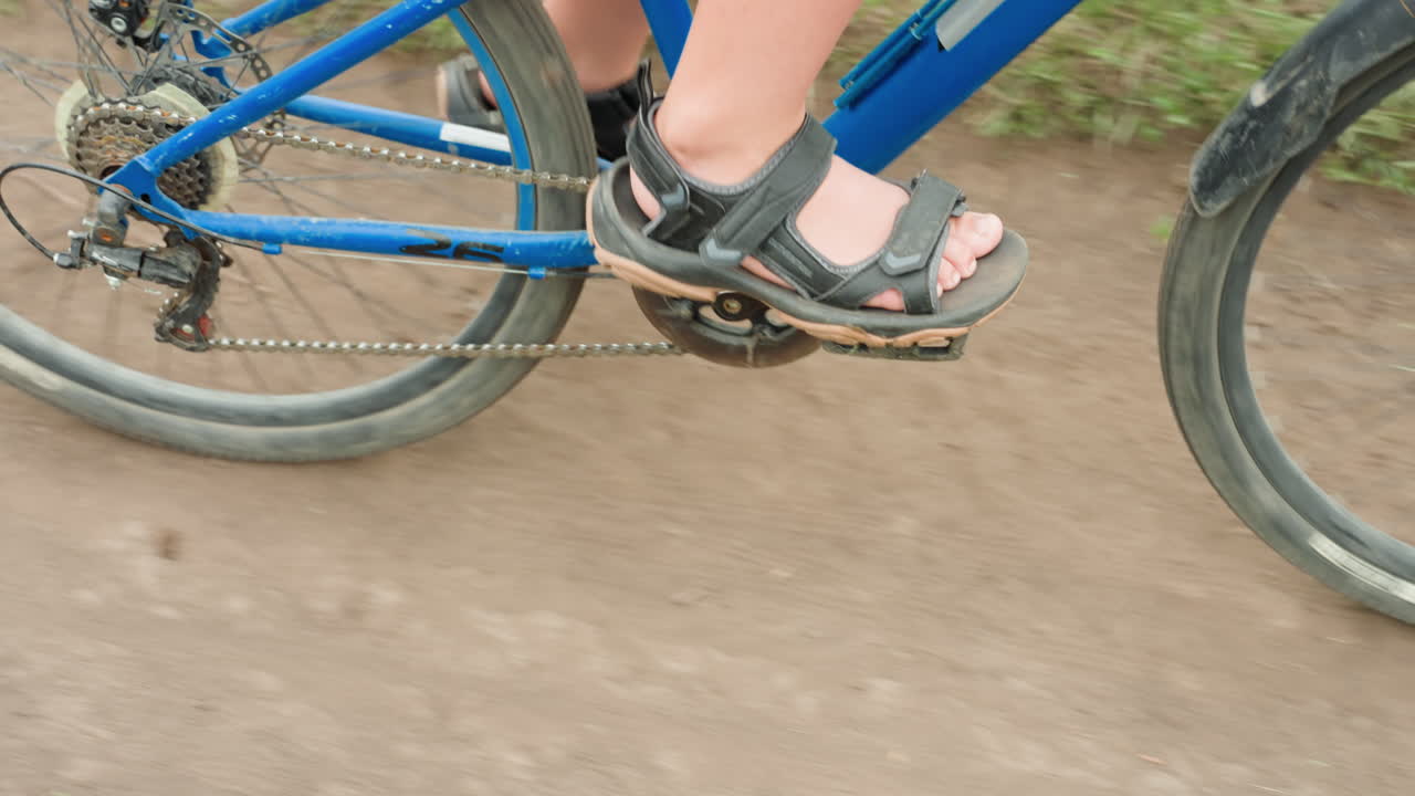 Child pedals rapidly on dusty dirt path, Youth cycling hurriedly through rugged countryside terrain, Energetic child speeds along dusty trail with gravel flying and tires kicking up dirt