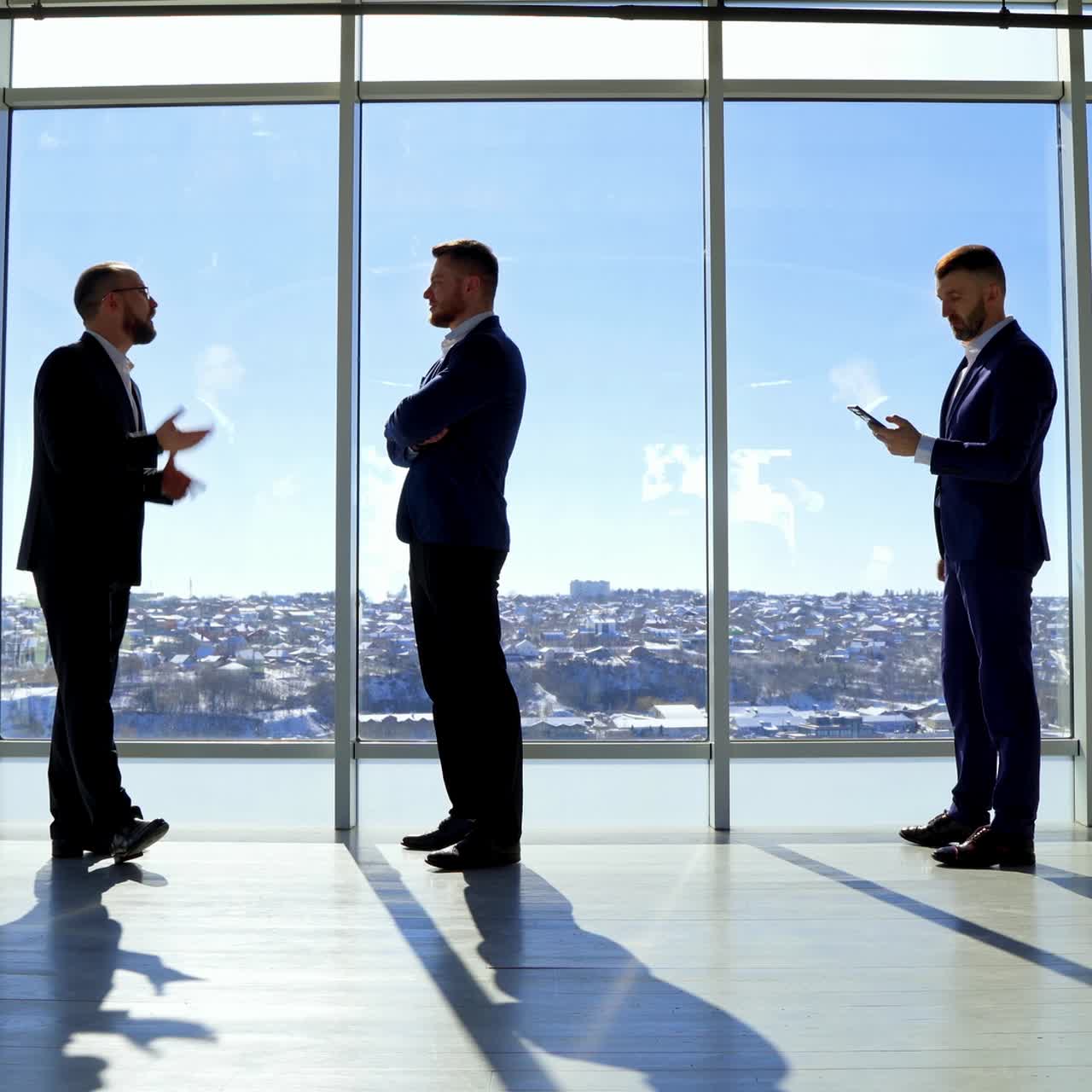 Businessmen portraits in full growth. Executive entrepreneurs in elegant costumes standing in the light office with a city view landscape through large windows