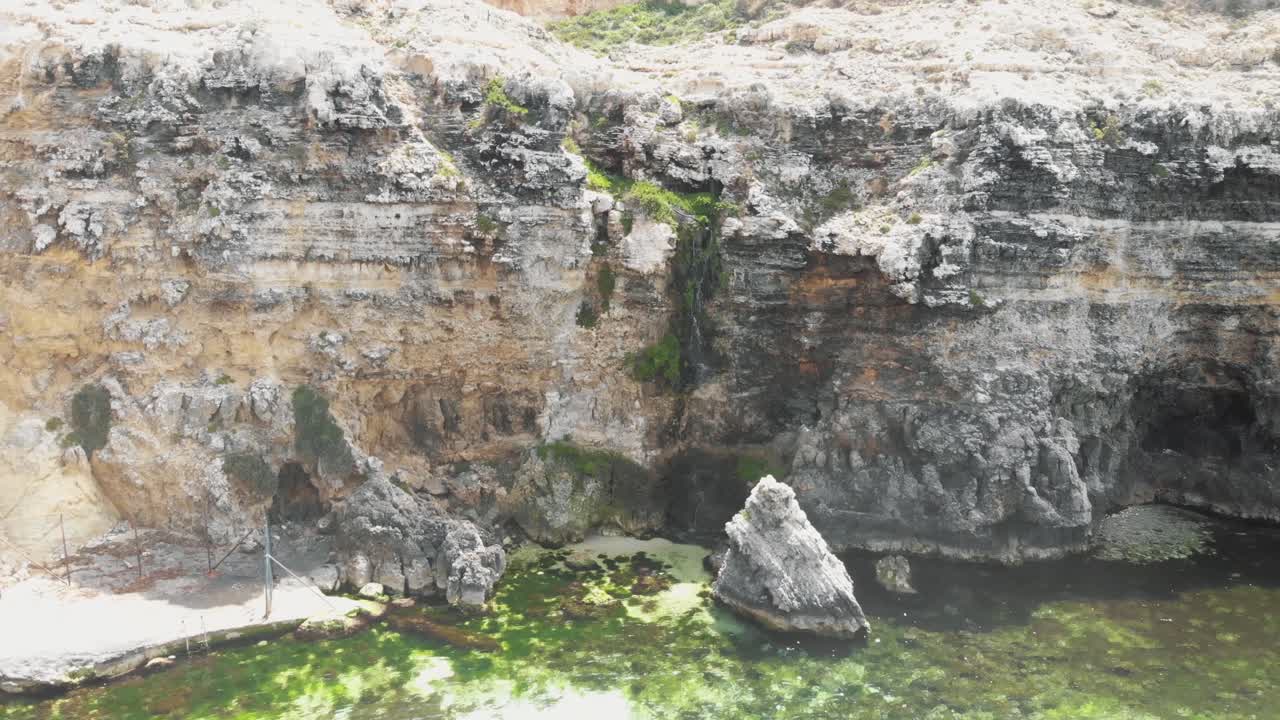 pequeña cascada en un acantilado rocoso que cae en cascada a través de las rocas hasta el mar mediterráneo en malta - toma aérea de revelación hacia atrás