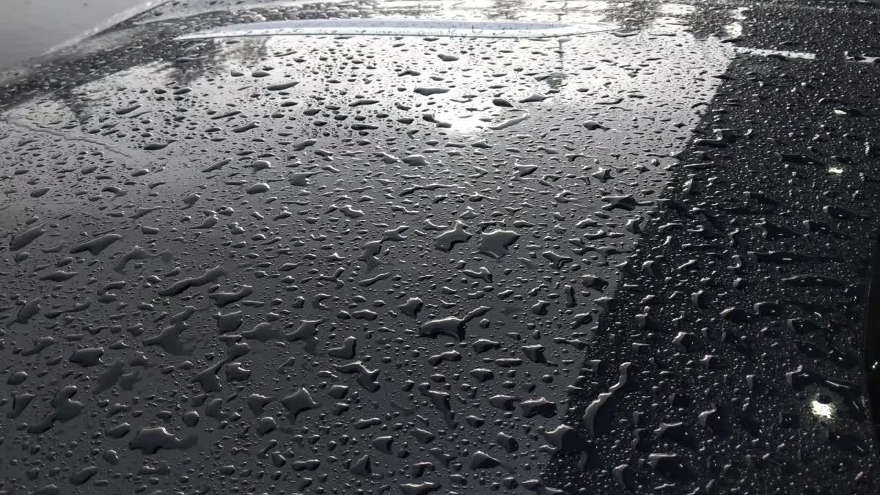 크롬 트림이 있는 진한 파란색 자동차의 보닛에 떨어지는 빗방울의 오른쪽에서 왼쪽으로 천천히 팬, 가로등과 나무가 있는 경우 반사