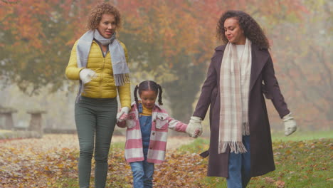 smiling multi-generation female family walk through autumn countryside swinging granddaughter in air